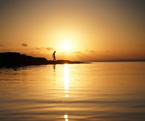 Person meditating peacefully outdoors at sunrise with golden light.